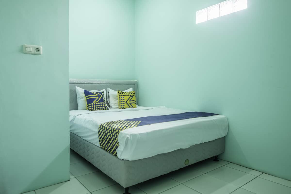 A single-bed room with a grey headboard, white bedding, and patterned pillows.