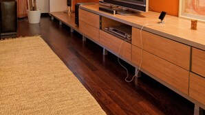 Un salon moderne avec un téléviseur à écran plat, des meubles en bois, une plante en pot et un grand tapis.