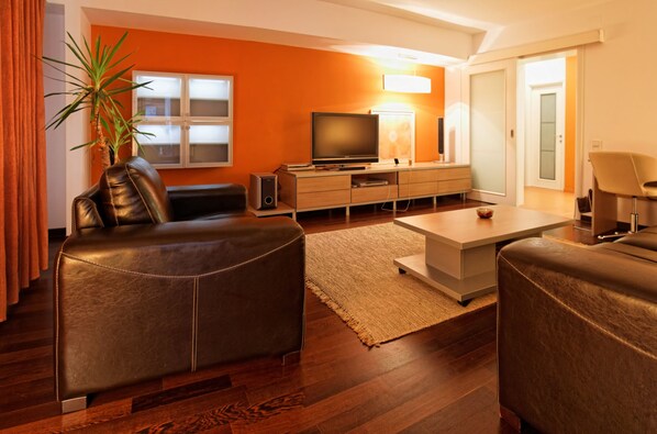 Una sala de estar moderna con un sofá de cuero, un televisor de pantalla plana, un mueble de madera y una planta grande.