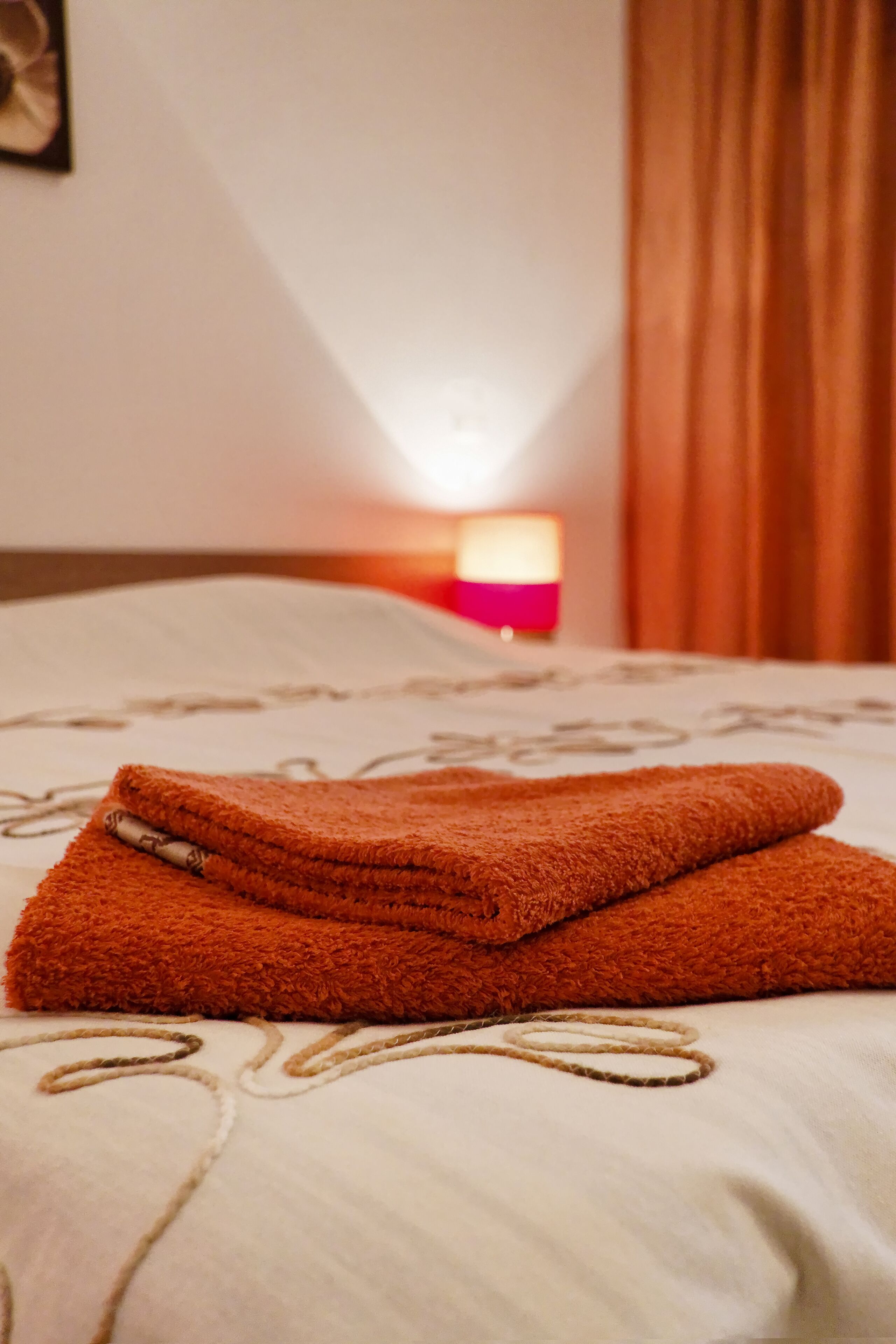 A neatly folded brown towel on a bed with a patterned bedspread.