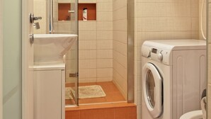 Une salle de bain compacte avec une douche à parois de verre, un lave-linge et des toilettes.