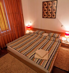 Una cama bien tendida con ropa de cama a rayas, una mesita de noche con lámpara y una obra de arte en la pared sobre la cama.