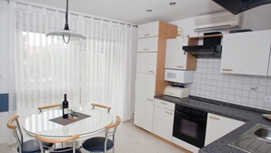 A modern kitchen with white cabinets, a black stove, and a microwave. There is a dining table with chairs and a hanging light fixture. - Apartments Spommy (Crikvenica)