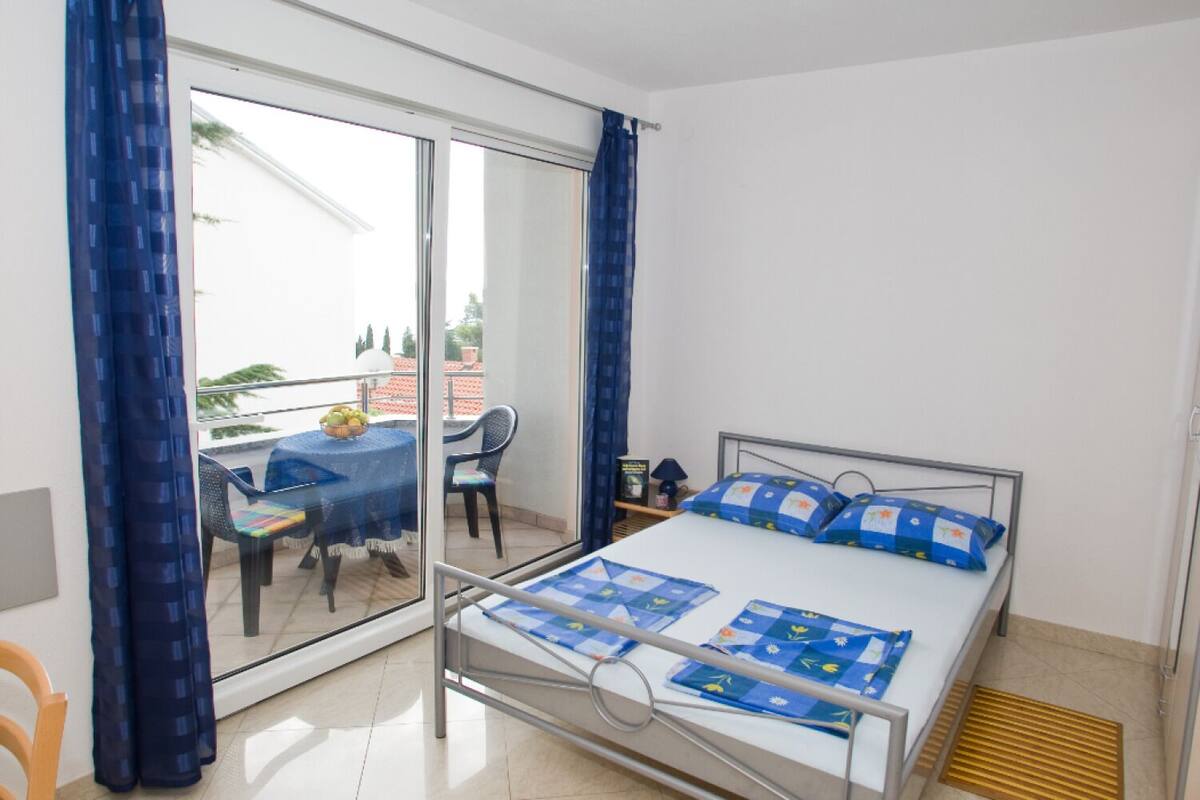 Quarto com cama, mesa pequena com cadeiras e varanda com mesa e cadeiras.