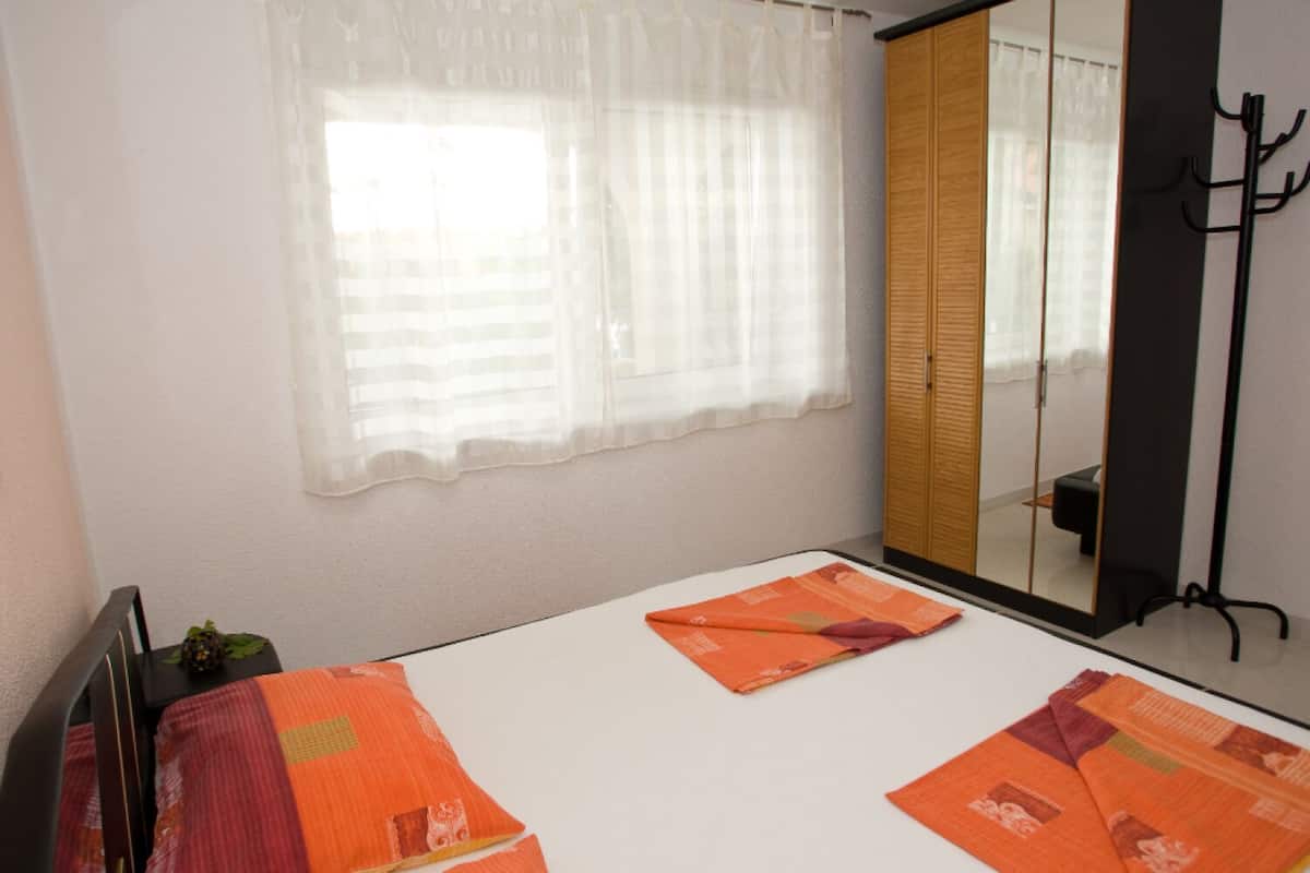 Quarto com cama, janela com cortinas leves, espelho e armário.
