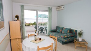A room with a round table, wooden chairs, a sofa with colorful cushions, a small side table, and a potted plant. - Apartments Spommy (Crikvenica)