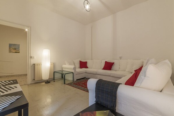 A living room with a white sofa, red cushions, a glass coffee table, a lamp, and a radiator.