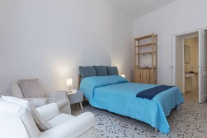 A bedroom with a bed, a chair, a nightstand, and a wooden ladder.