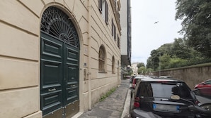 Une rue étroite bordée de voitures garées, un immeuble avec une porte verte et un oiseau qui vole dans le ciel.