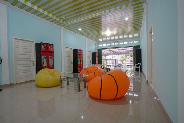 A hallway with a tiled floor, green-striped ceiling, and doors leading to rooms. There are orange bean bags and a table with chairs.