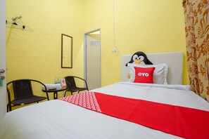 A hotel room with a bed, a small table with bottles, two chairs, a hanging laundry rack, and a door. - OYO 1991 Alam Lestari Homestay (Palembang)
