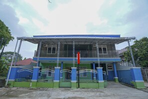 A two-story building with a balcony, a gated entrance, and a red flag. - OYO 1991 Alam Lestari Homestay (Palembang)