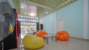 A room with a fan, a glass table, orange bean bag chairs, and a door.