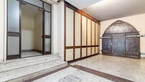 Una entrada de edificio con una serie de escalones que conducen a una puerta, un suelo de baldosas y una gran estructura arqueada a la derecha.