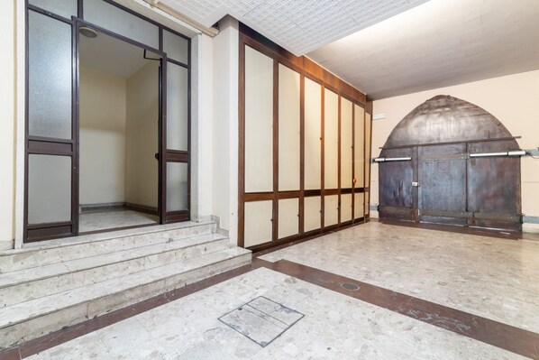 Una entrada de edificio con una serie de escalones que conducen a una puerta, un suelo de baldosas y una gran estructura arqueada a la derecha.