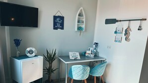 A compact room with a desk, two chairs, a small fridge, a potted plant, and a TV mounted on the wall. - ORCA Hotel am Elbschloss (Dresden)