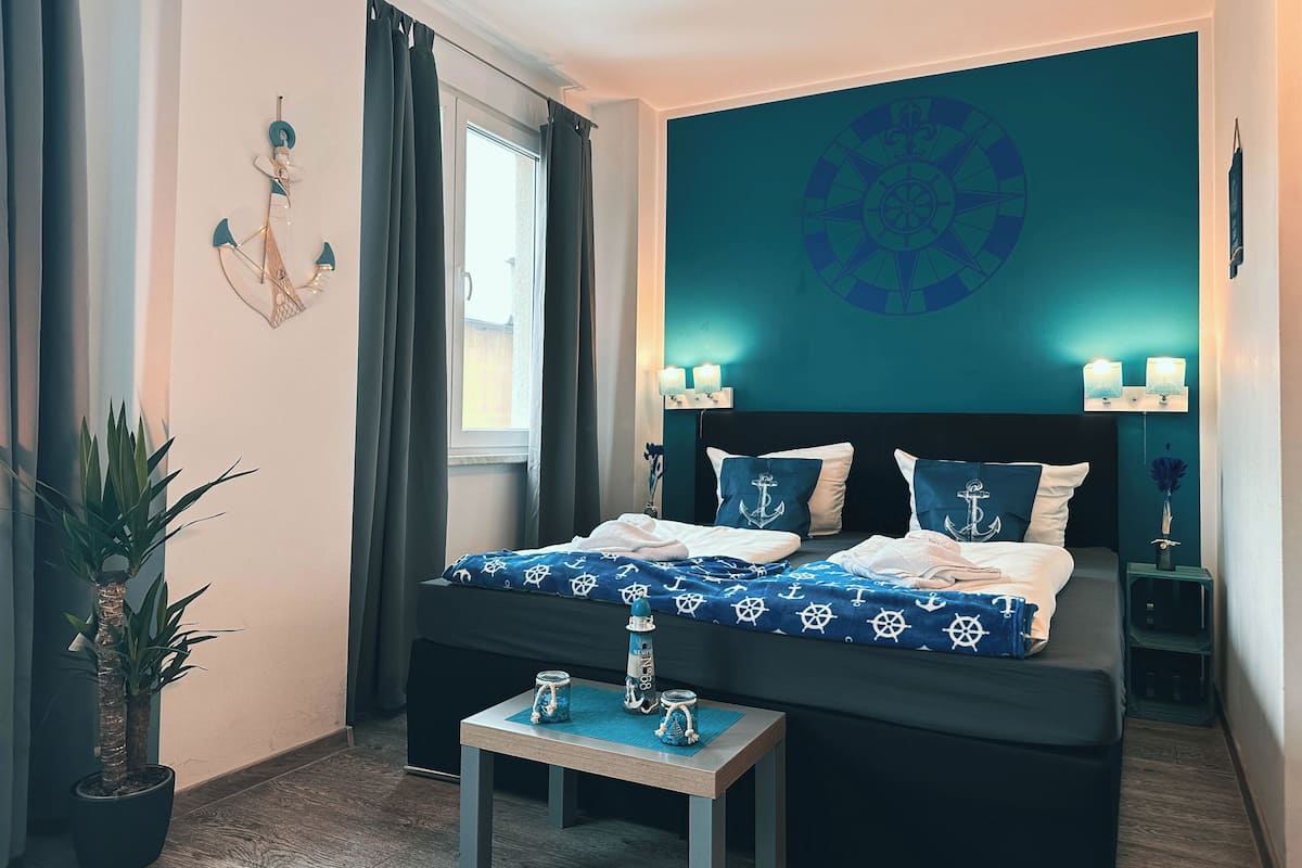 Une chambre à coucher comprenant un lit, une petite table, une plante en pot et un mur décoré sur le thème de la marine.