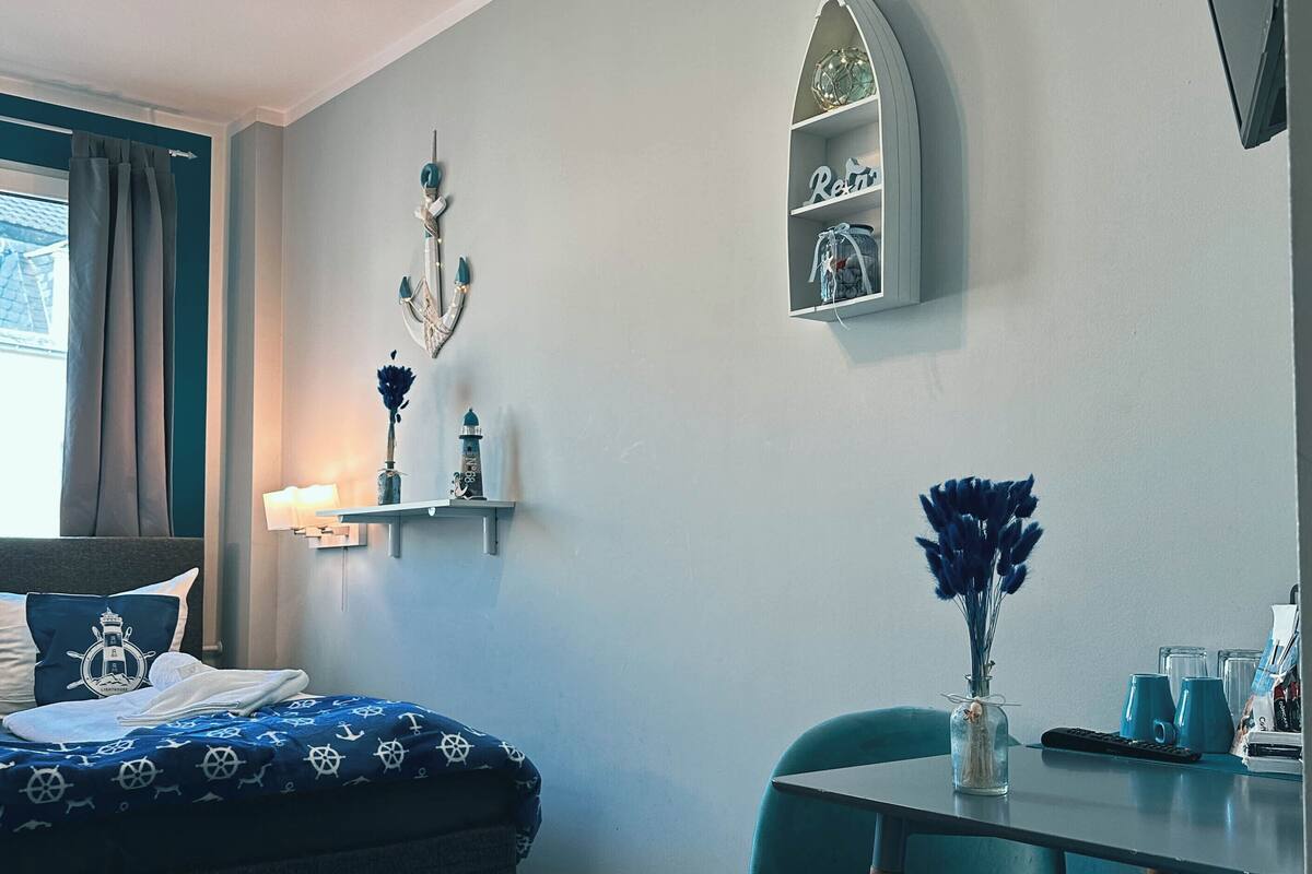 Une chambre à coucher comprenant un lit, un bureau, une chaise, une étagère avec une horloge et un vase avec des fleurs.