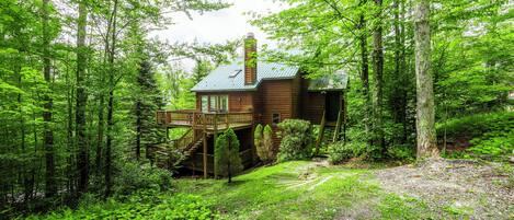 A wooden cabin with a deck, surrounded by dense forest.