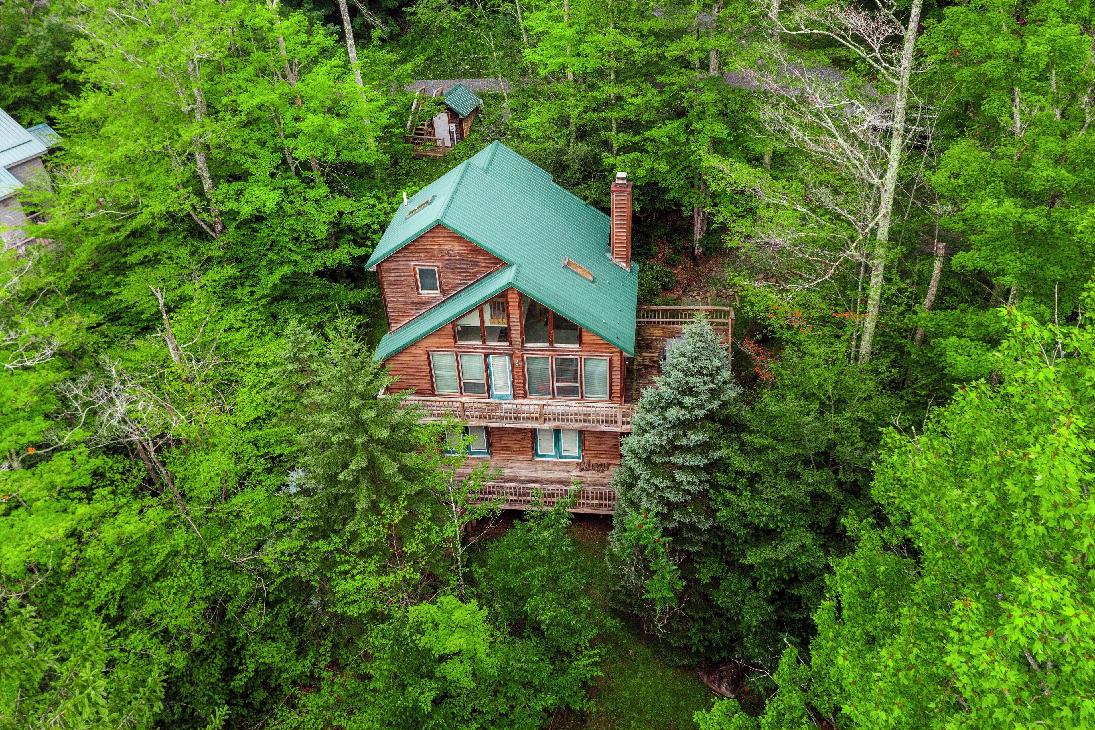 A two-story wooden house surrounded by dense green forest.