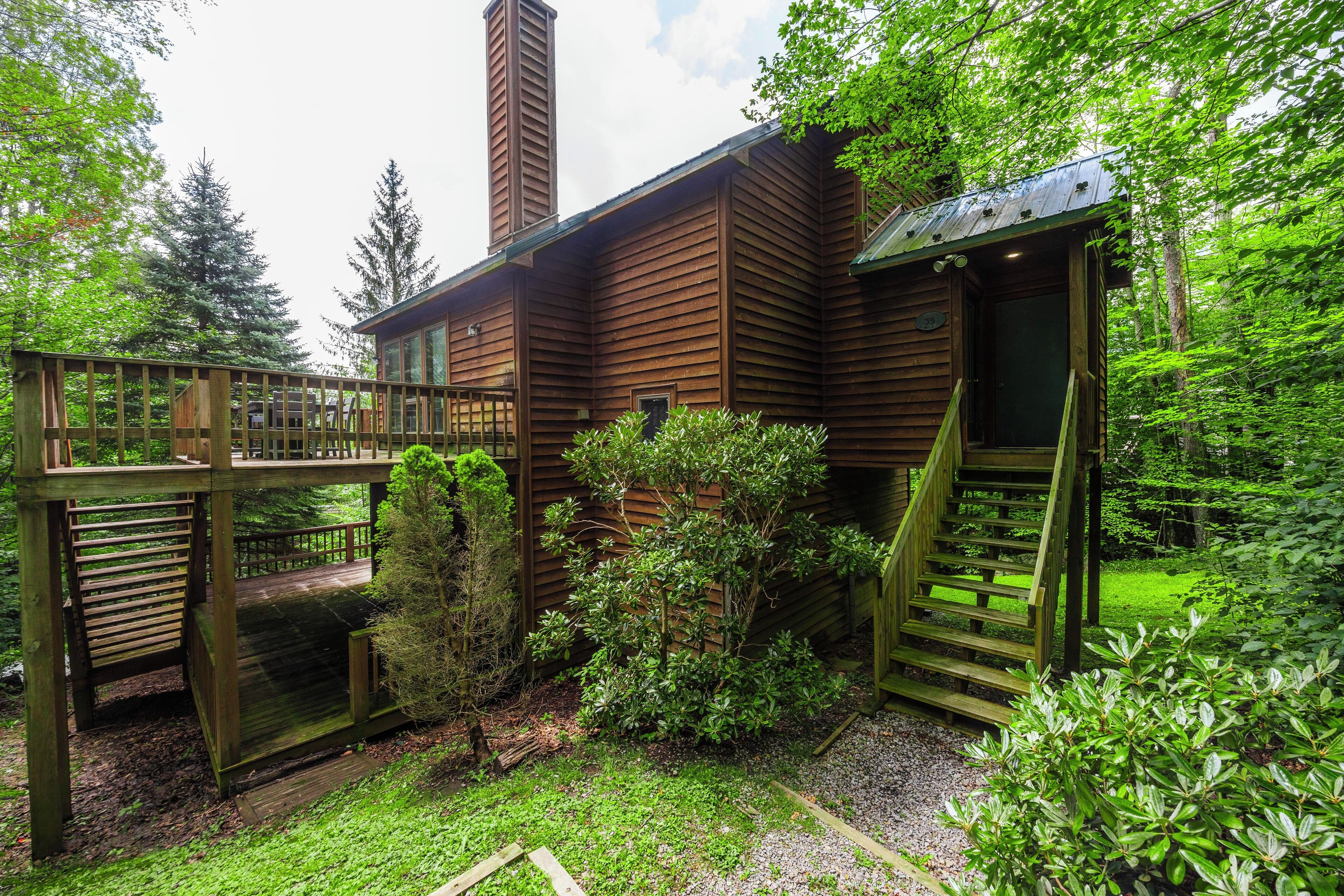 A wooden cabin with a deck, surrounded by lush greenery and trees.