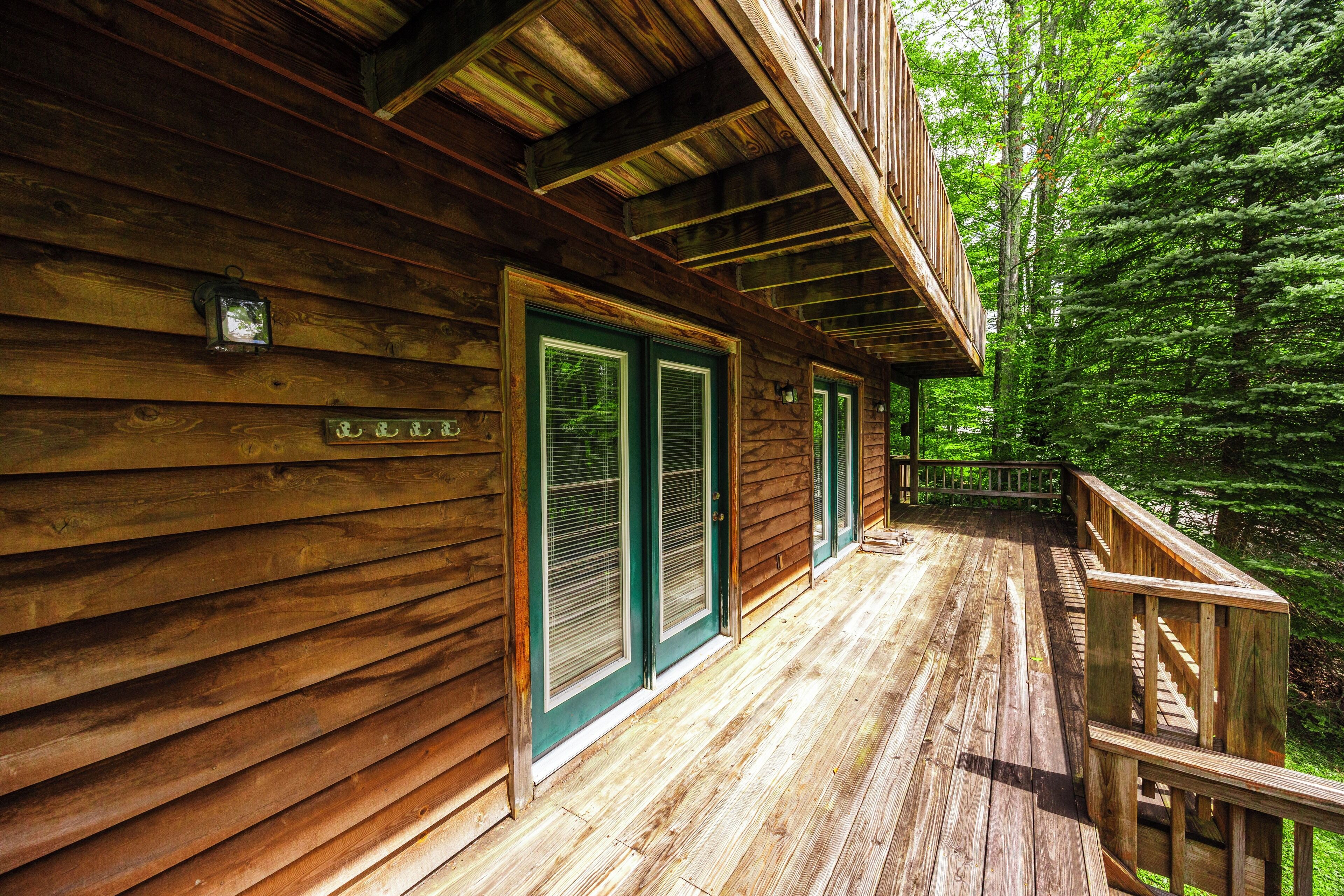 A wooden cabin with a porch, green shutters, and a wooden deck.