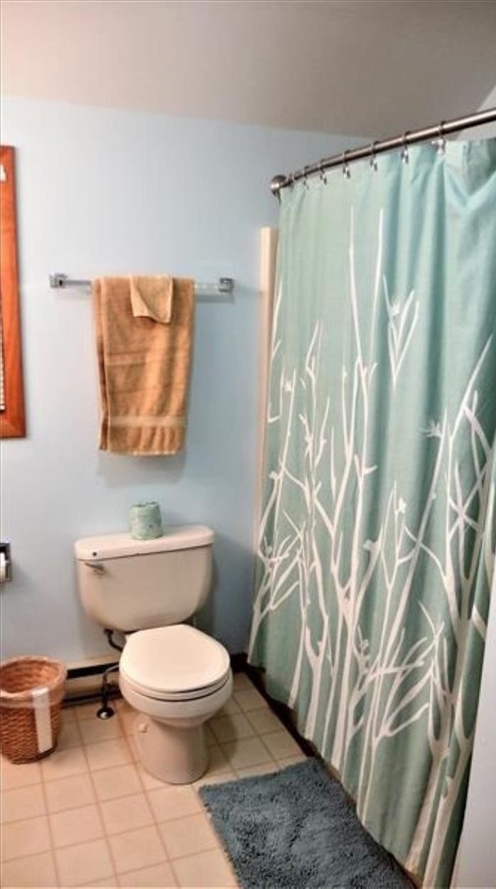 A bathroom with a toilet, a towel rack with a towel, and a shower curtain with a bamboo pattern.