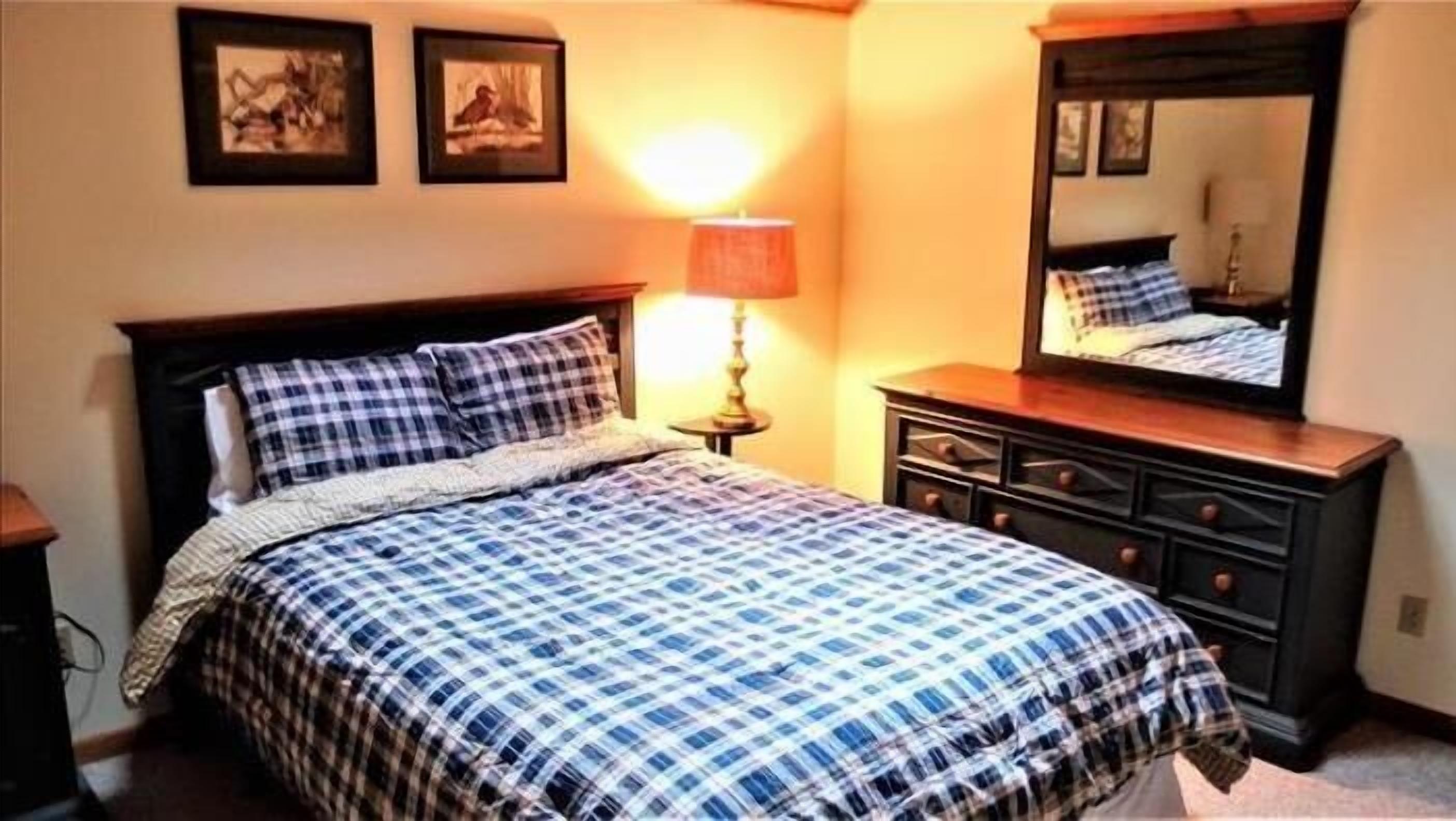 A bedroom with a bed, a dresser, a lamp, and two framed pictures on the wall.