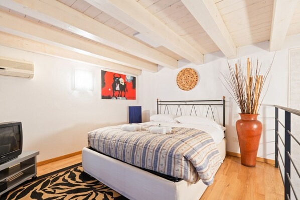 Ein Schlafzimmer mit einem Bett, einem Fernseher, einer wandmontierten Klimaanlage, einem Wanddekor und einer Vase mit Zweigen.