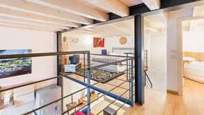 A modern interior with exposed wooden beams, a staircase, and a living area with a sofa and a painting. - GuestHost - Lovely loft apartment just 350m from Lodi M3 stop (Milano)