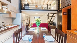 A dining area with a wooden table set for four, a vase with flowers, and a staircase leading to an upper level. - GuestHost - Lovely loft apartment just 350m from Lodi M3 stop (Milano)