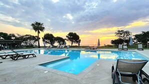 Piscina con sillones de descanso y vista al atardecer.