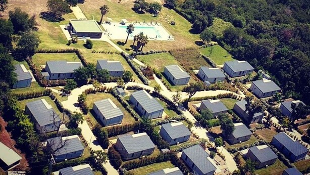 Vista aérea de una zona residencial costera con casas dispuestas en un patrón de cuadrícula, una playa y un amplio espacio abierto con piscina.