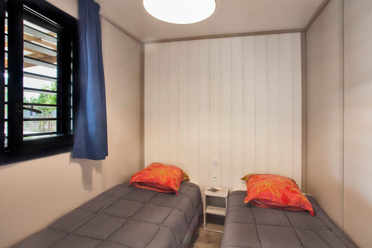 Una habitación pequeña con dos camas individuales, una ventana con cortina y una pared blanca con diseño de paneles de madera.