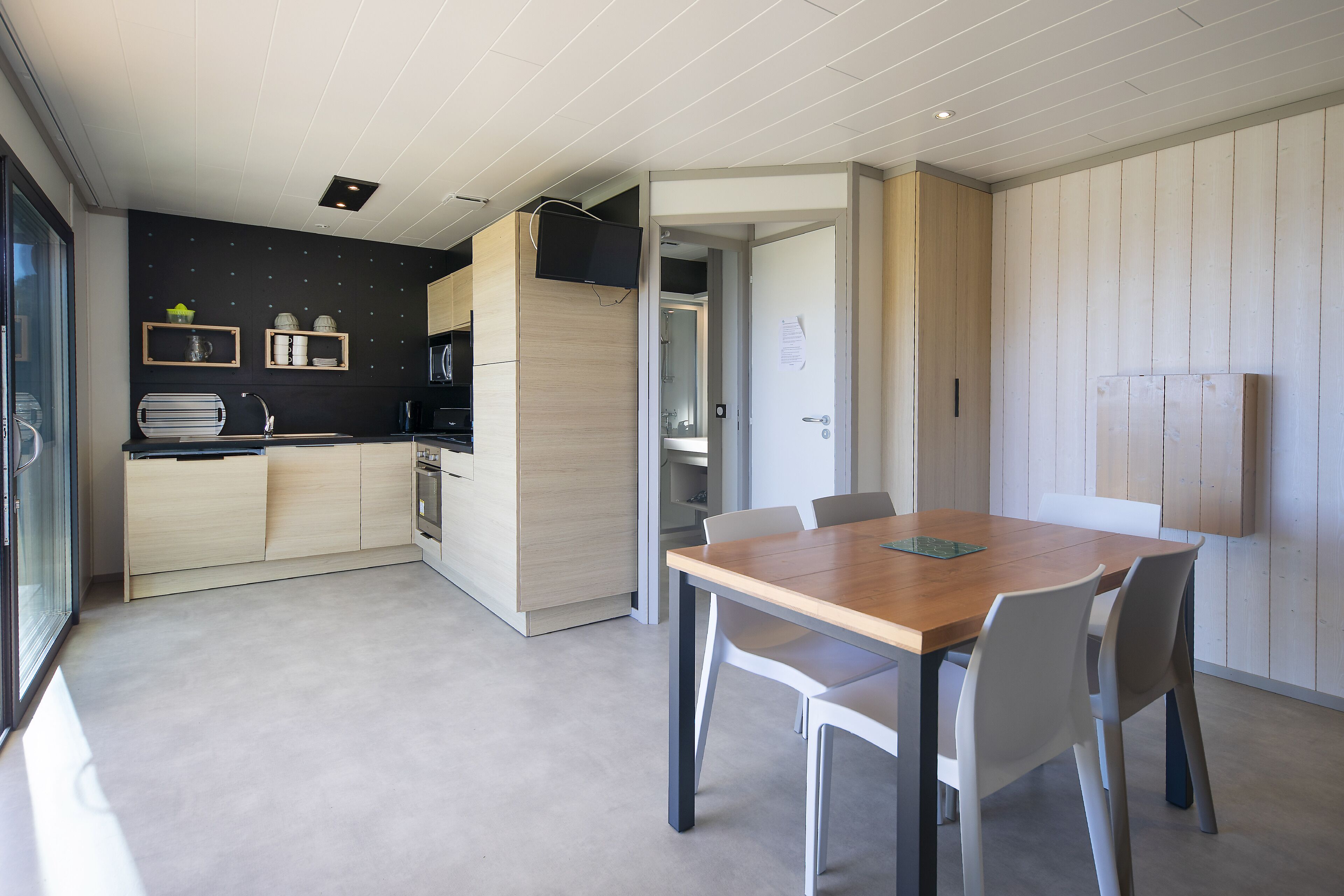 A modern kitchen with wooden cabinets, a built-in microwave, and a dining area with a wooden table and white chairs.