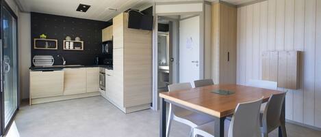 A modern kitchen with wooden cabinets, a built-in microwave, and a dining area with a wooden table and white chairs.