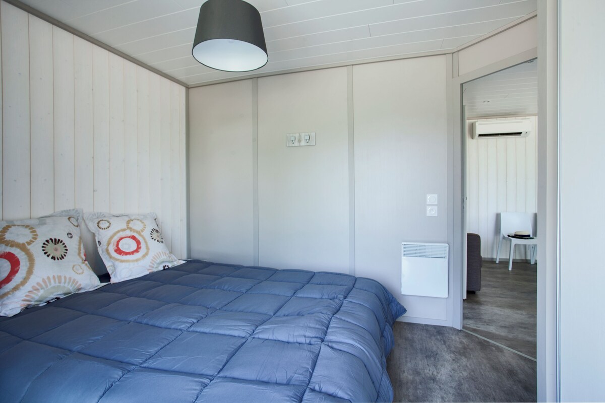 Une chambre avec une couvre-lit bleue, des murs blancs, un luminaire au plafond et un appareil de climatisation blanc.