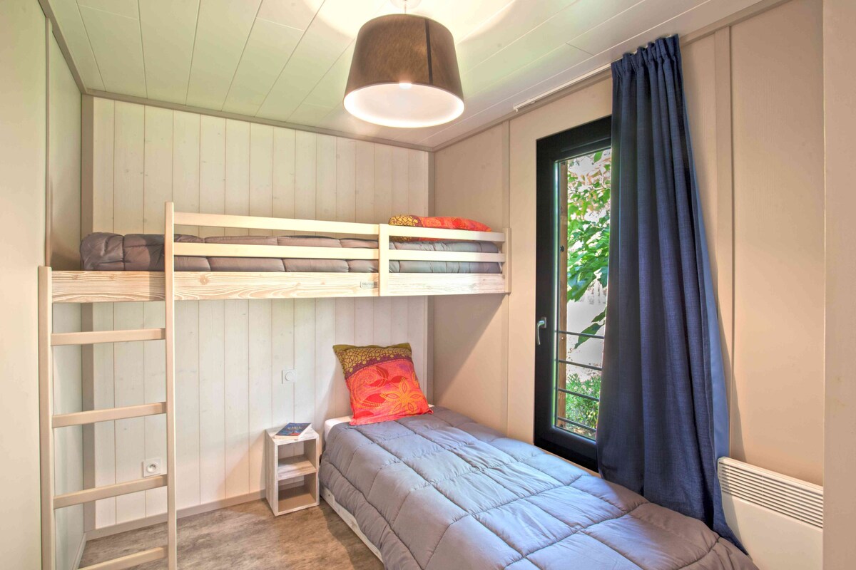 A bunk bed room with a ladder, a desk, and a window with curtains.
