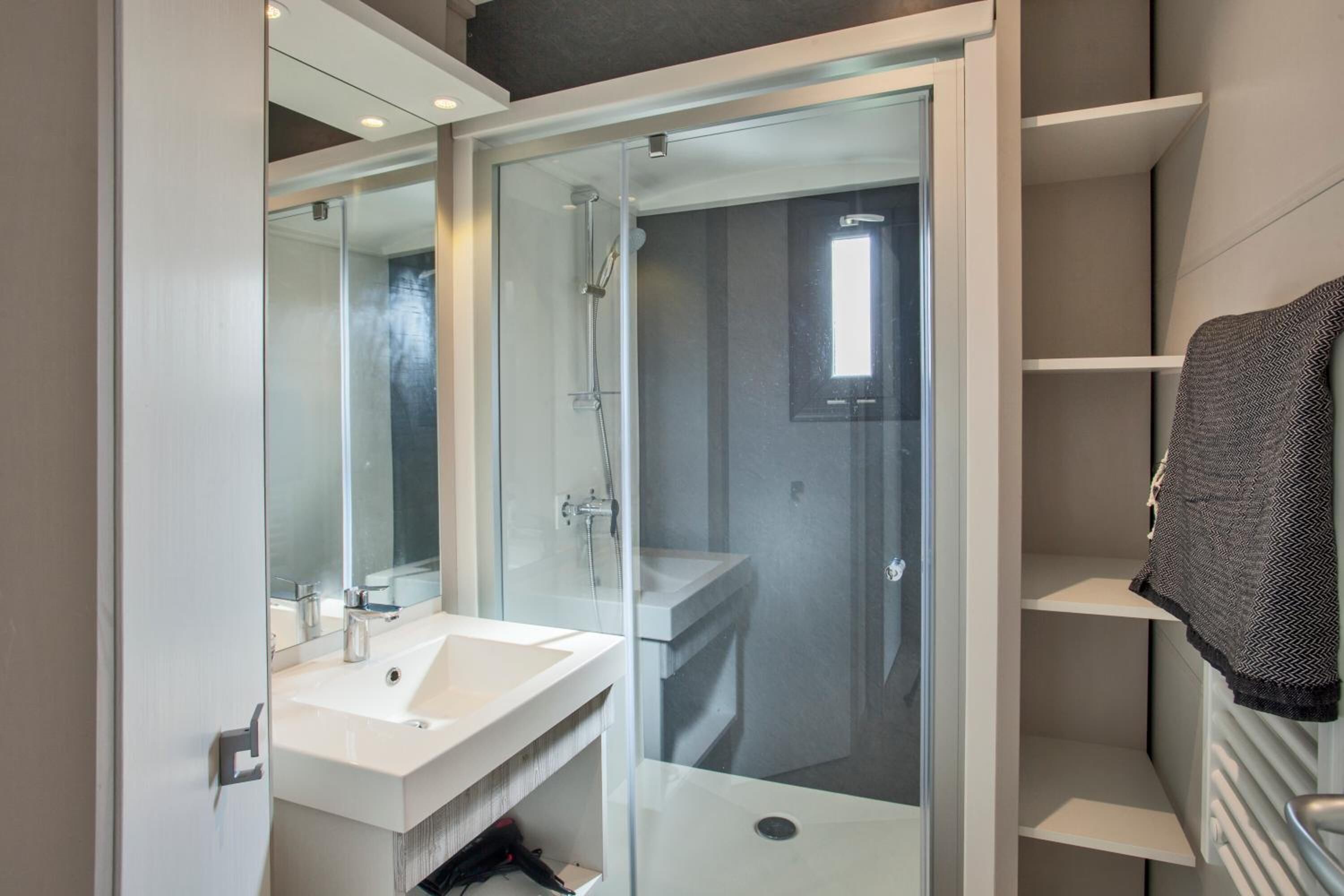 Un baño moderno con ducha de vidrio, lavamanos blanco y un perchero para toallas.