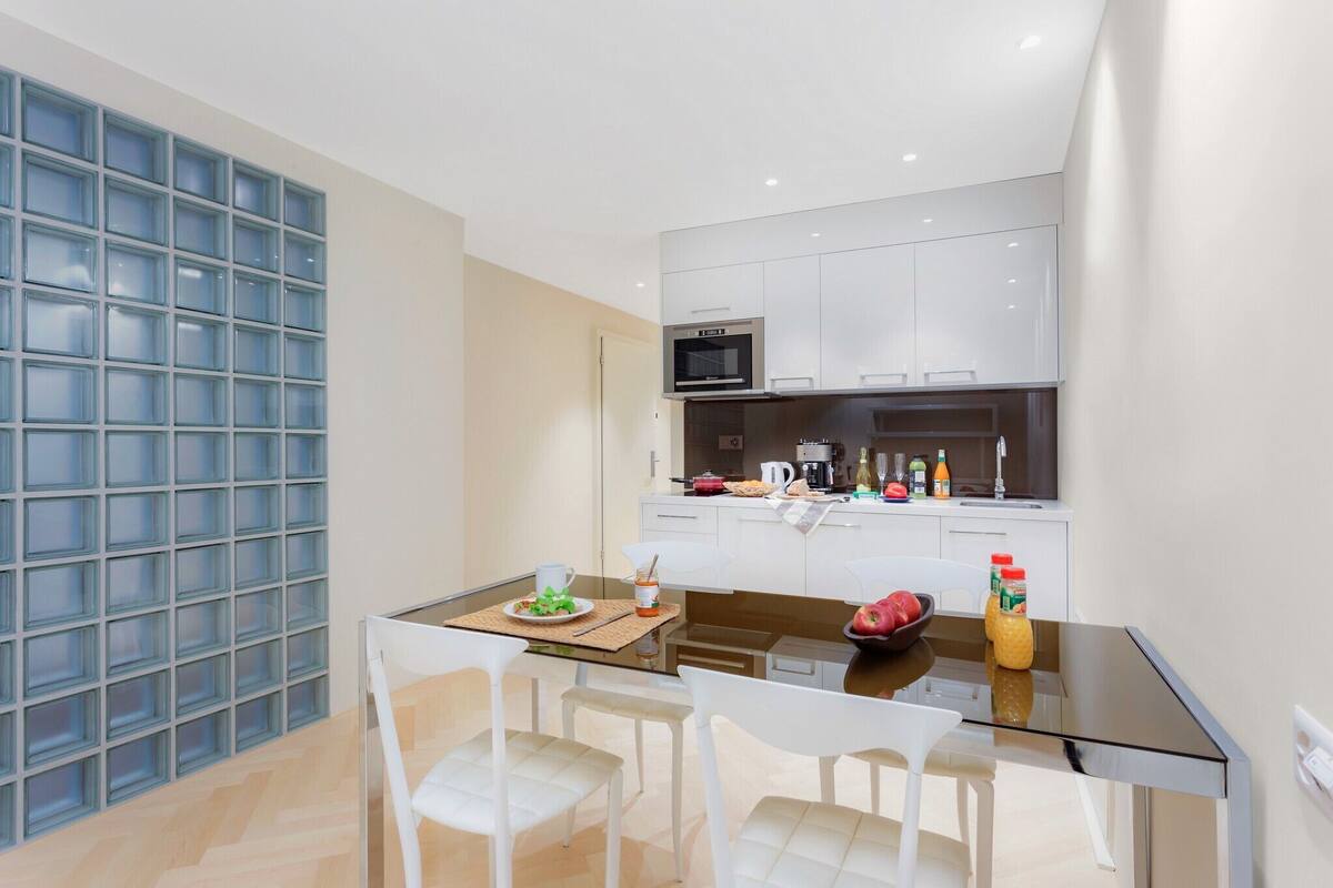 A modern kitchen with white cabinets, a microwave, and a dining area with a glass table and white chairs.