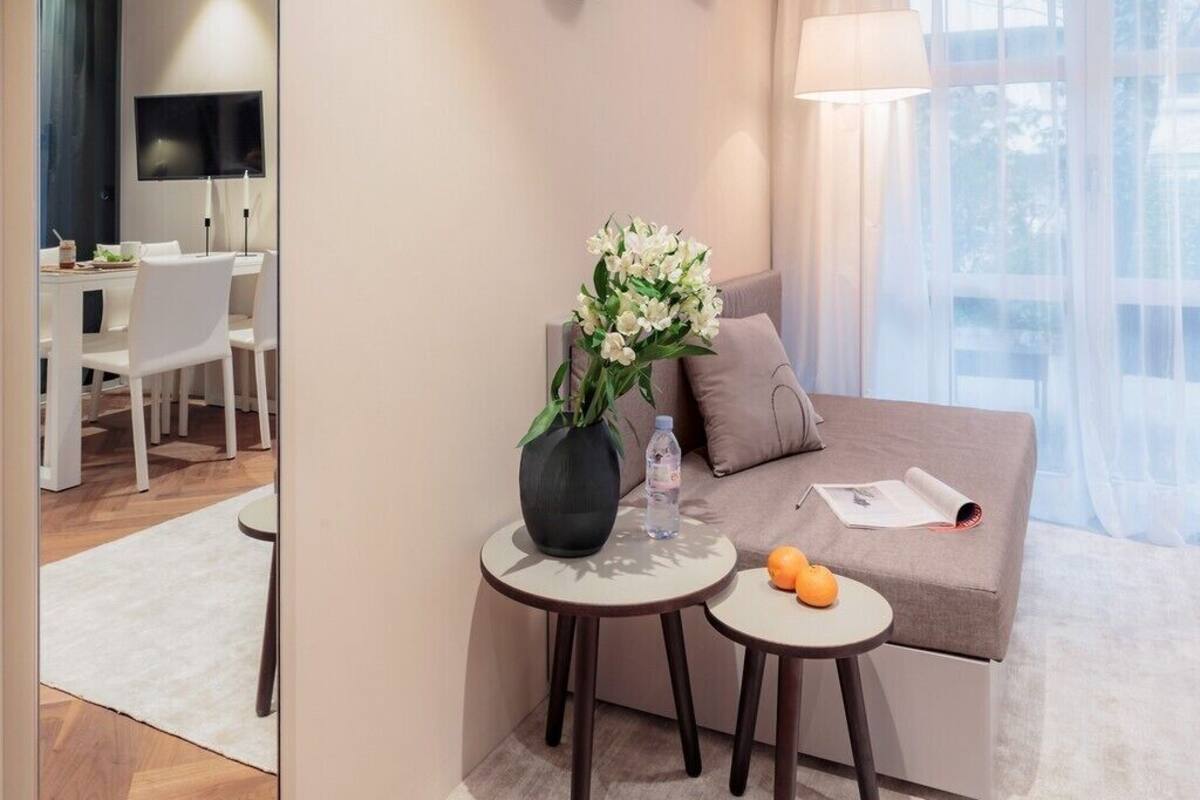 A modern hotel room with a sofa, two small tables, a mirror, and a TV.
