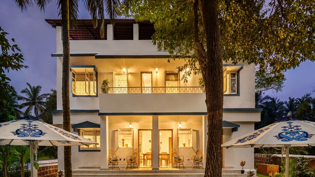 A two-story building with a balcony, outdoor seating, and a well-maintained garden. - amã Stays & Trails, Braganza House - Goa (Candolim)
