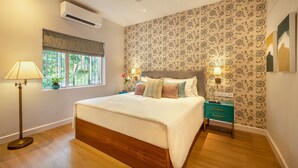 A bedroom with a large bed, a nightstand, a lamp, a window with a view, and a ceiling fan. - amã Stays & Trails, Braganza House - Goa (Candolim)