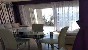 Un coin repas avec une table et des chaises en verre, un canapé et une vue sur l’extérieur grâce à de grandes fenêtres.
