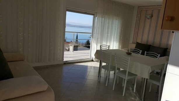 Un salon moderne comprenant un coin repas, un canapé, une table avec des chaises et une vue sur la mer, visible à travers une porte vitrée.