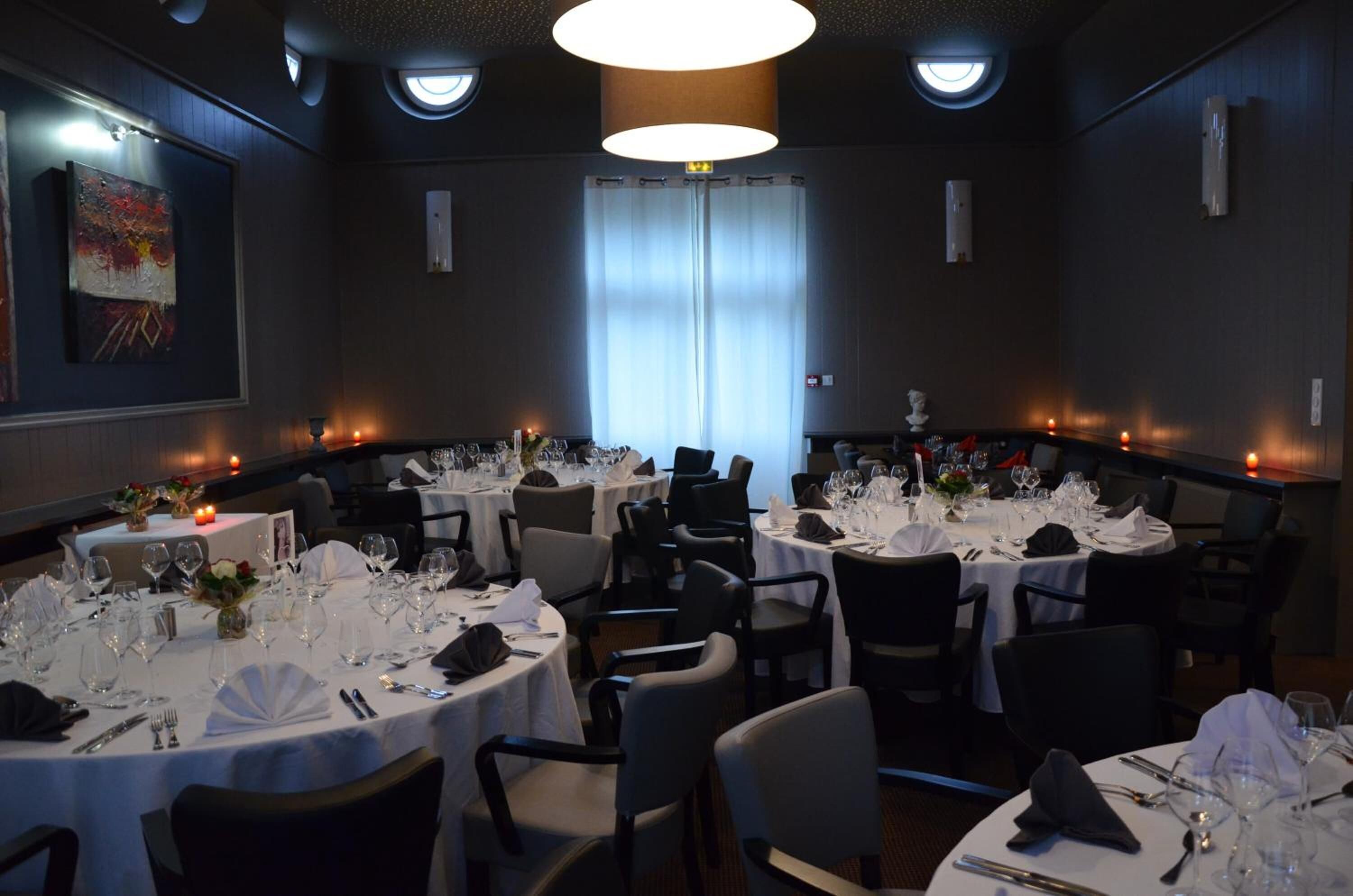 Un salón de conferencias con mesas redondas dispuestas para un evento formal, con manteles blancos, sillas y cristalería.