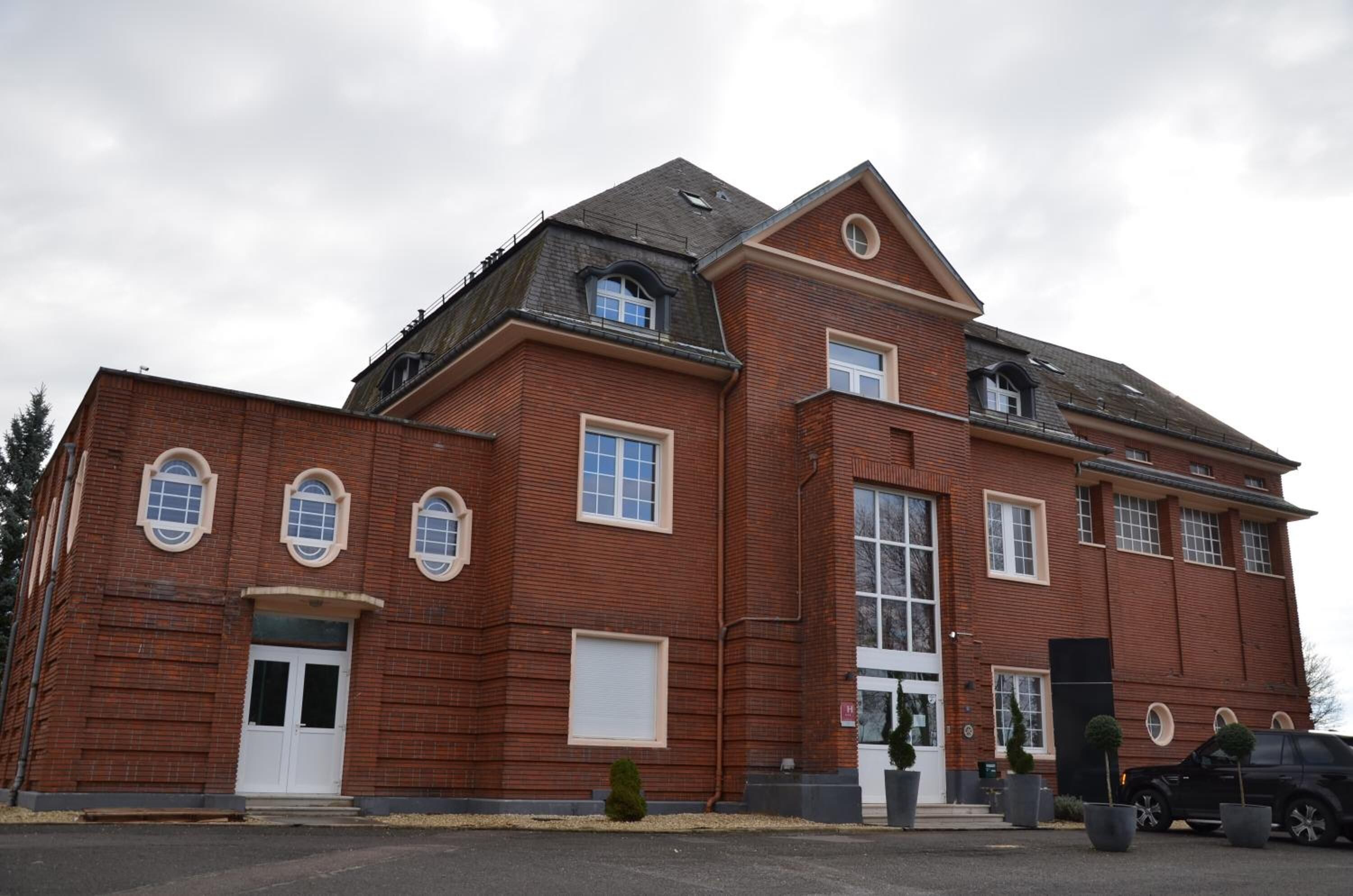 A large, red brick building with a symmetrical facade, large windows, and a prominent entrance.