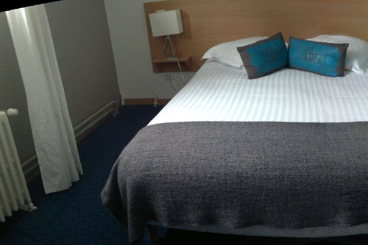 A hotel room with a bed, two bedside lamps, a door, and a radiator.