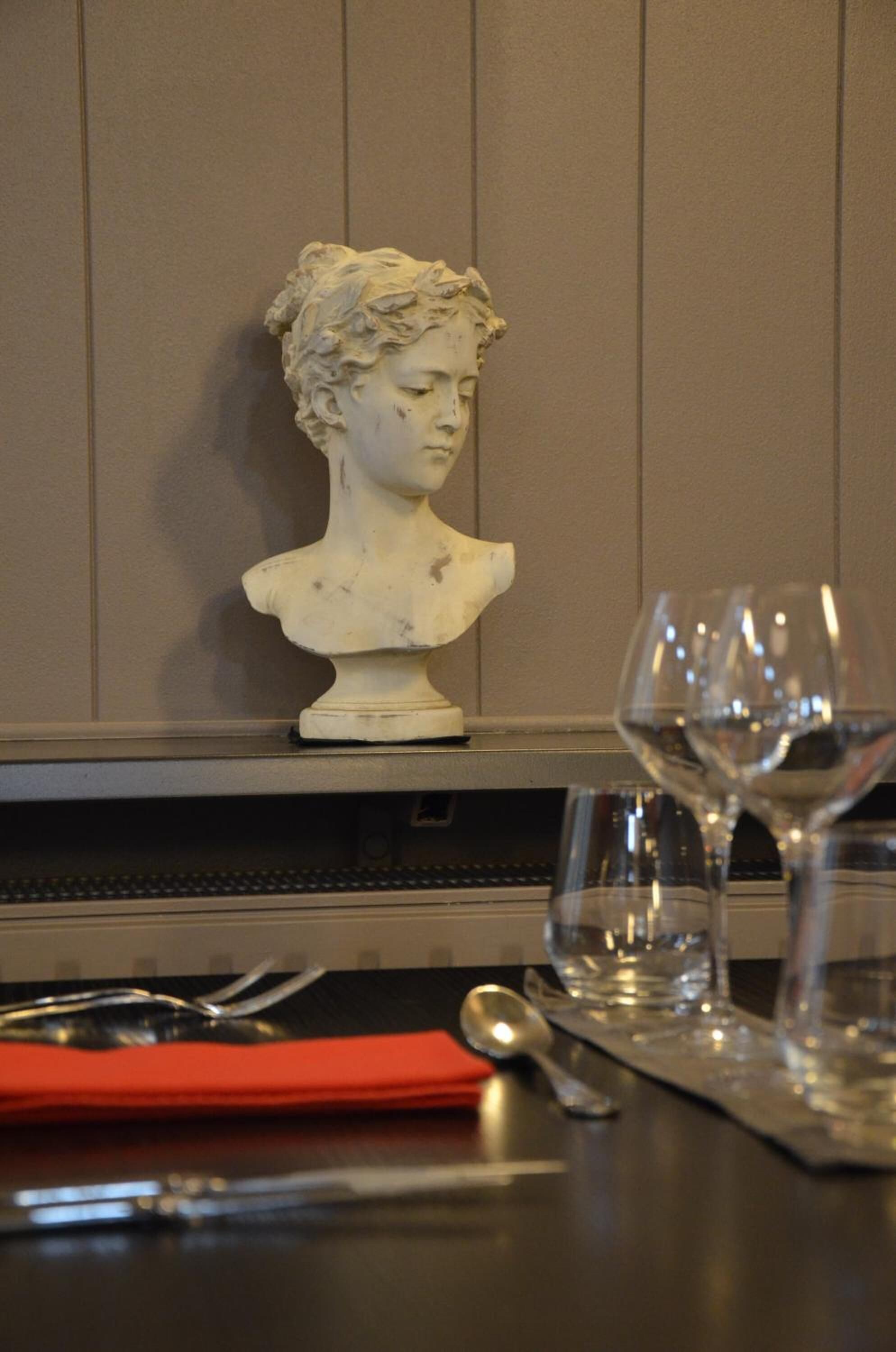 A bust sculpture on a wall, a wine glass, and a dining table with cutlery.