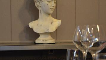 A bust sculpture on a wall, a wine glass, and a dining table with cutlery.